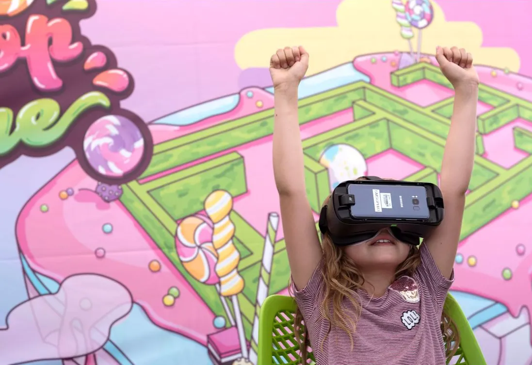 A little girl wearing a VR headset with her arms up in celebration.